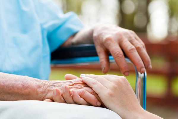 woman in wheelchair having hand held by caretaker